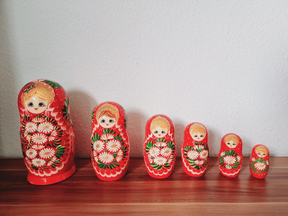 Auf einem Holztisch stehen sechs rote kleiner werdende Matroschka Puppen.