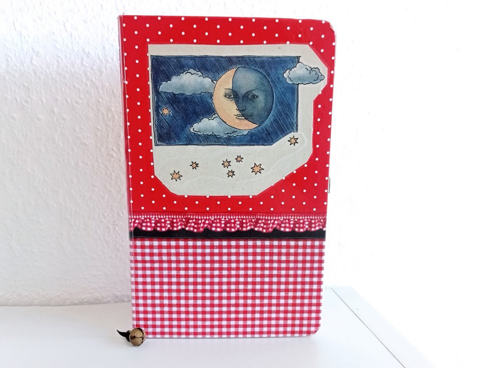 Red diary with a picture of a moon stands on white table.